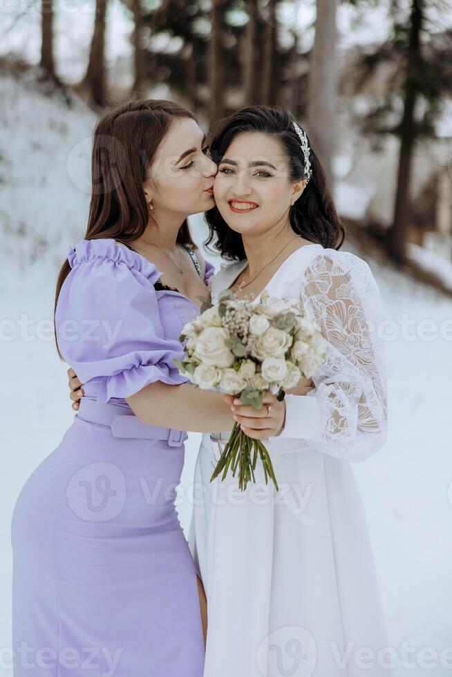 Two women are hugging each other and one of them is holding a bouquet of flowers. The scene is set in a snowy environment, which adds a sense of warmth and intimacy to the moment photo