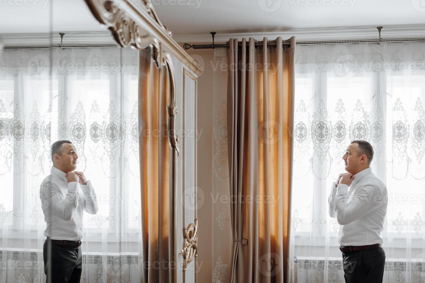 A man is getting ready for a wedding and is adjusting his tie. The image is a reflection of him in a mirror photo