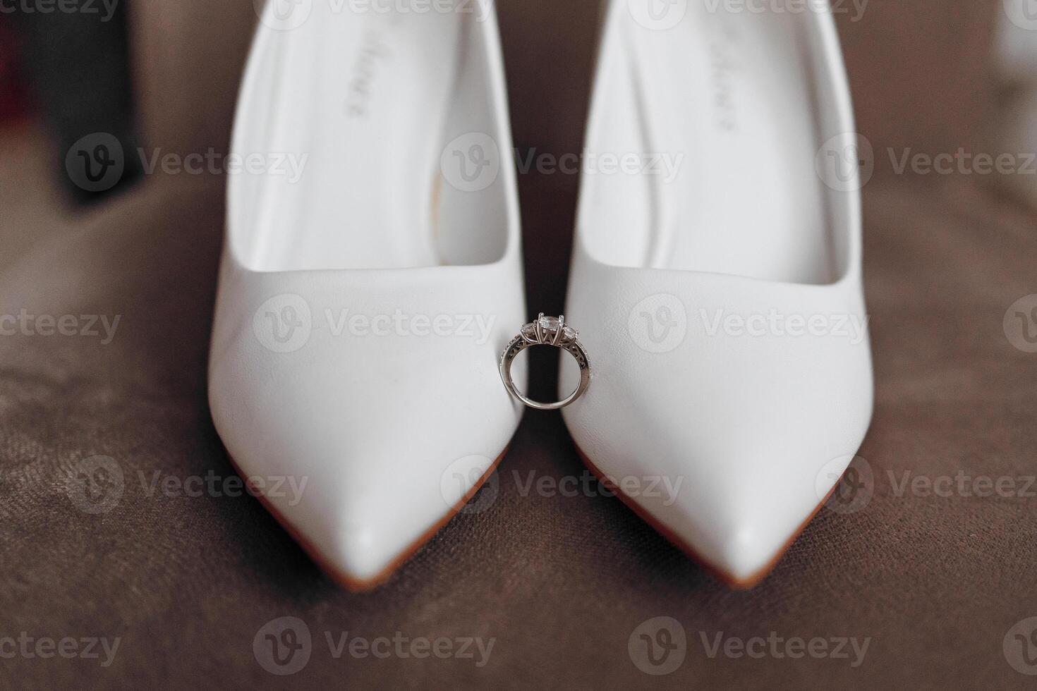 A pair of white shoes with a ring on the toe. The shoes are on a brown surface photo