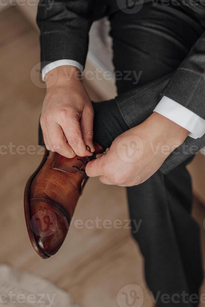 A man is putting on his shoes. The shoes are brown and the man is wearing a suit photo