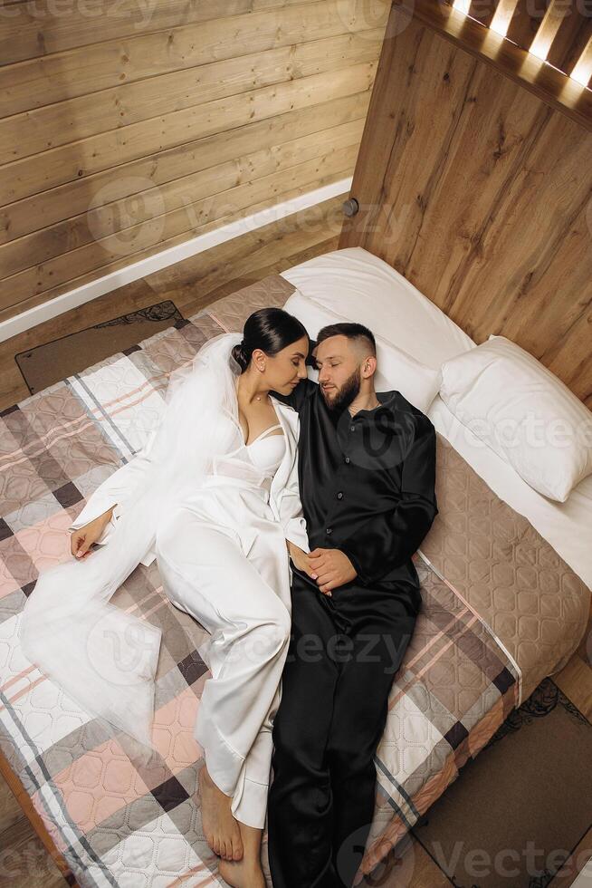 A man and woman are lying on a bed, holding hands and looking at each other. Scene is romantic and intimate photo