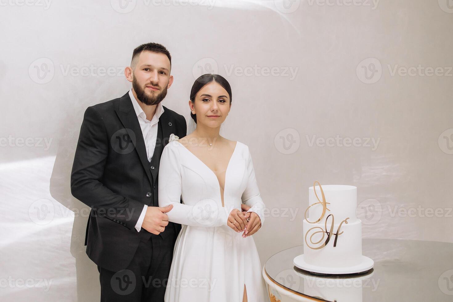 A man and woman are posing for a picture in front of a wedding cake with the letter H on it photo