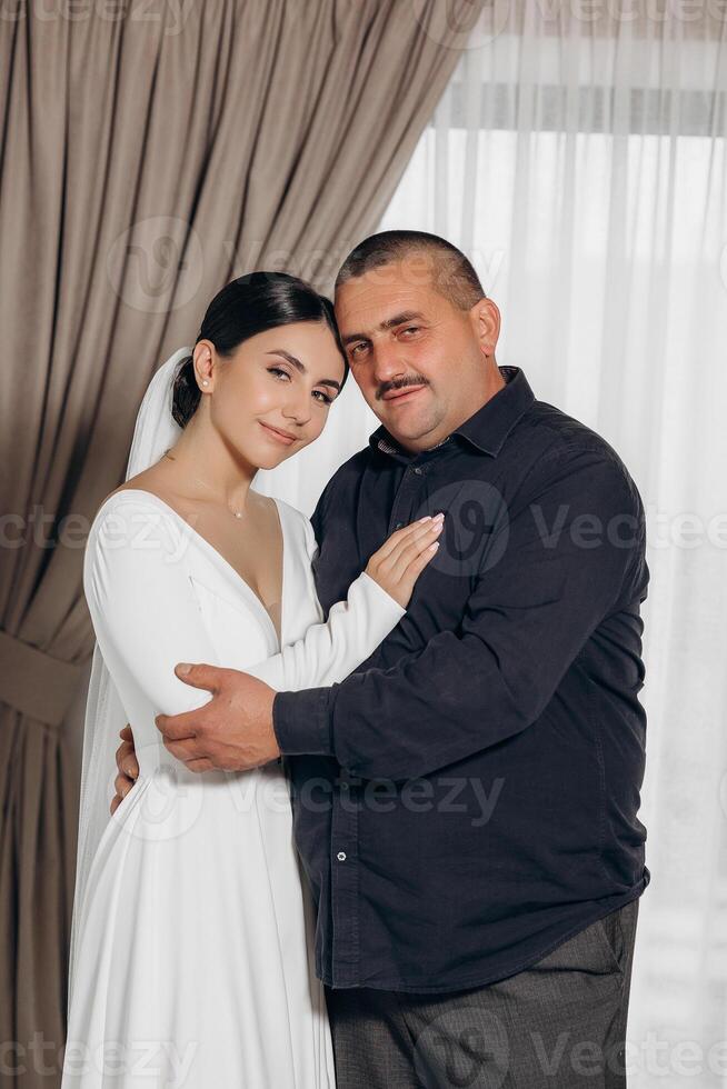 A man and a woman are hugging each other. The man is wearing a black shirt and the woman is wearing a white dress photo