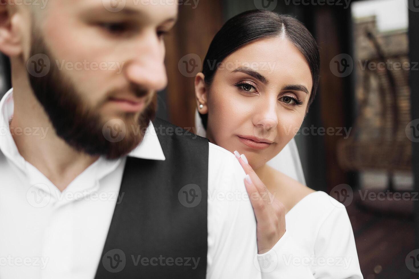 A man and a woman are standing close to each other, with the woman looking at the camera. The man is wearing a suit and the woman is wearing a wedding dress. Scene is romantic and intimate photo