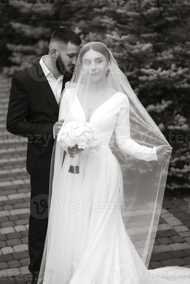A bride and groom are standing on a brick walkway, with the bride wearing a veil and the groom holding a bouquet photo