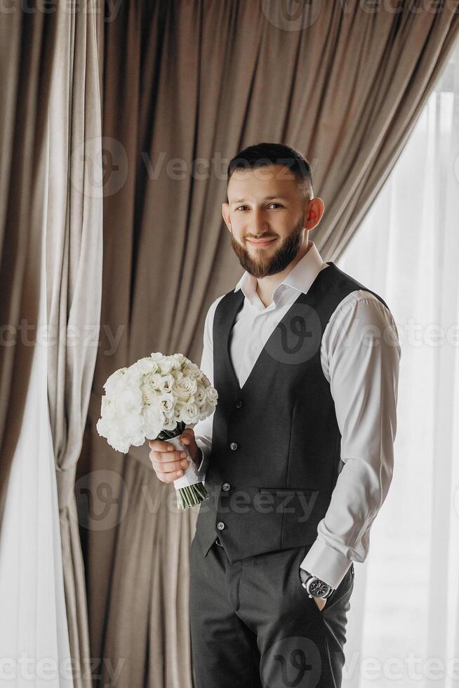 A man in a black vest and white shirt is holding a bouquet of white flowers. Concept of elegance and sophistication, as the man is dressed in a formal attire and the flowers are a symbol of love photo