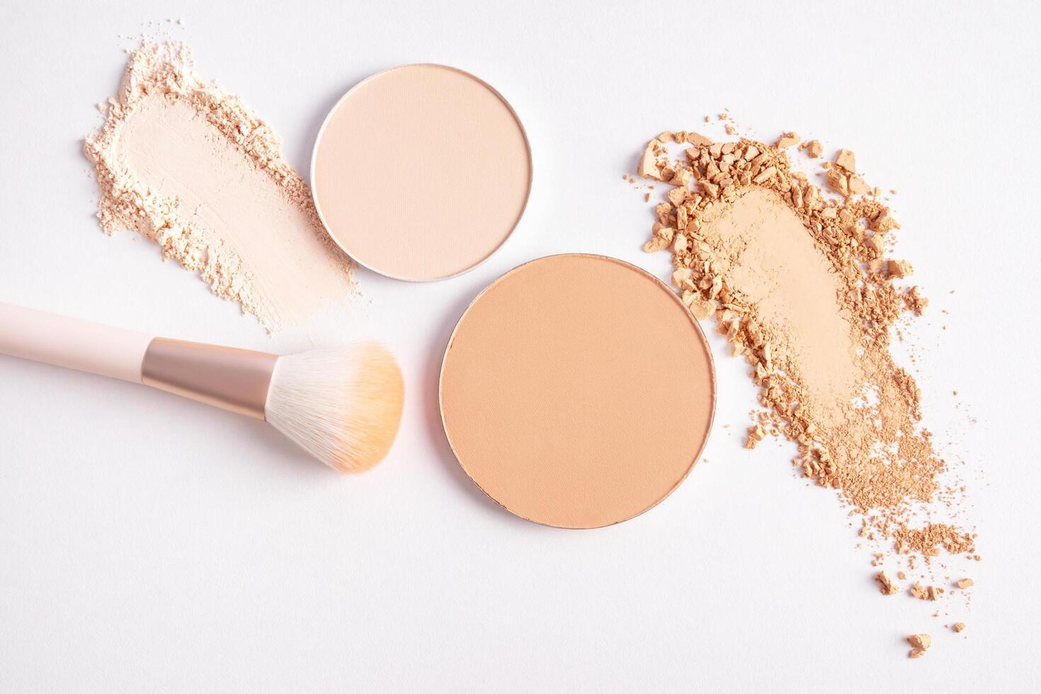 cosmetic background with texture samples of compact and loose powder in different tones. A chic makeup brush. top view. white background. photo