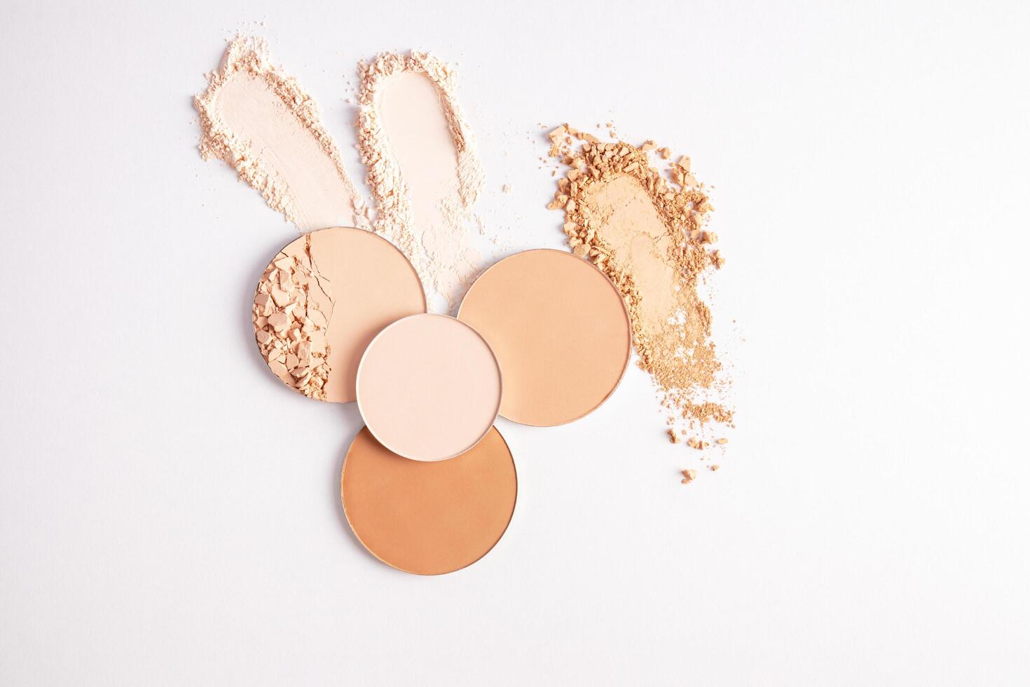 Several round blocks of compact powder in different tones and three beautiful samples of loose powder on a white background. top view. texture. photo