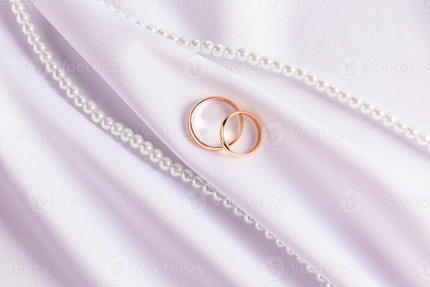 Two classic gold wedding rings on a white satin background with beautiful pleats and a string of pearl beads. Wedding design concept. invitation photo