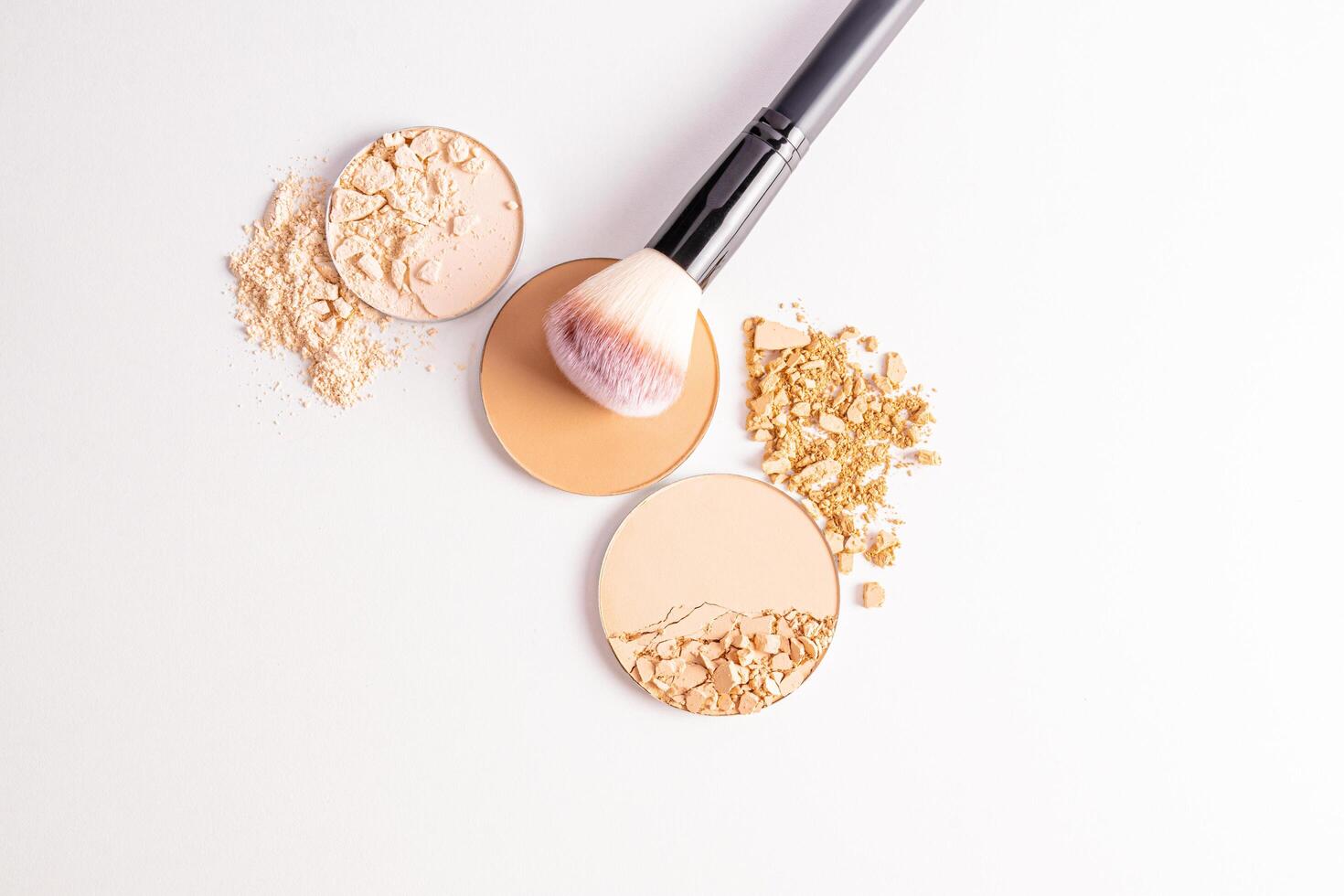 cosmetic background with texture samples of compact and loose powder in different tones. A chic makeup brush. top view. white background. photo