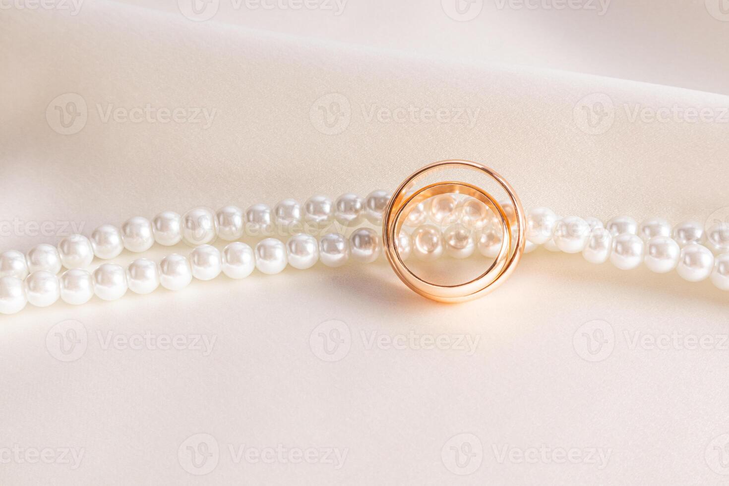 Two elegant gold wedding rings against a string of pearl beads and beige satin. stylish wedding background. postcard. invitation. front view. photo