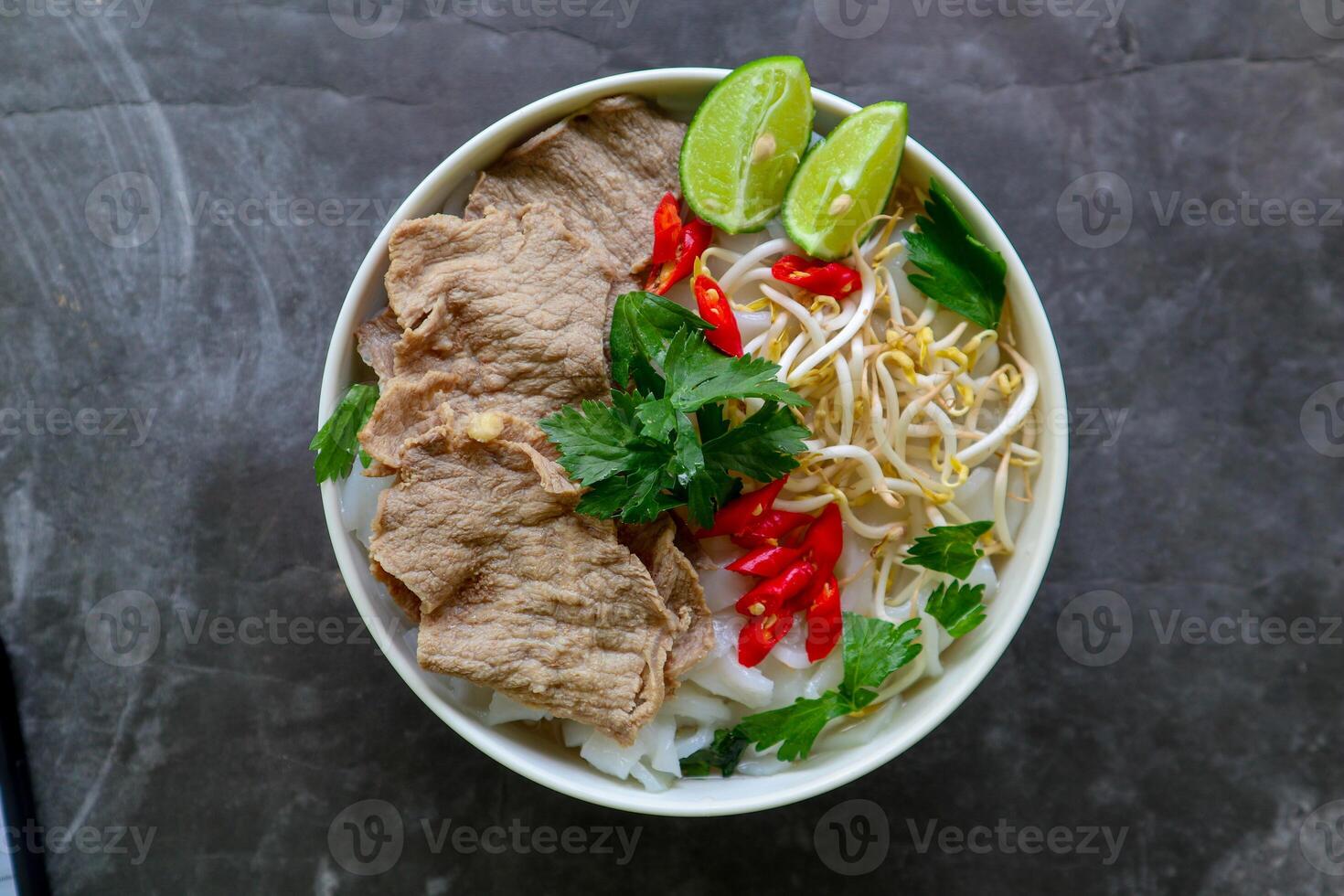 A Bowl Pho Bo traditional Soup with beef, rice noodles, ginger, lime, chili pepper in bowl. Close up. Vietnamese cuisine served on black background photo