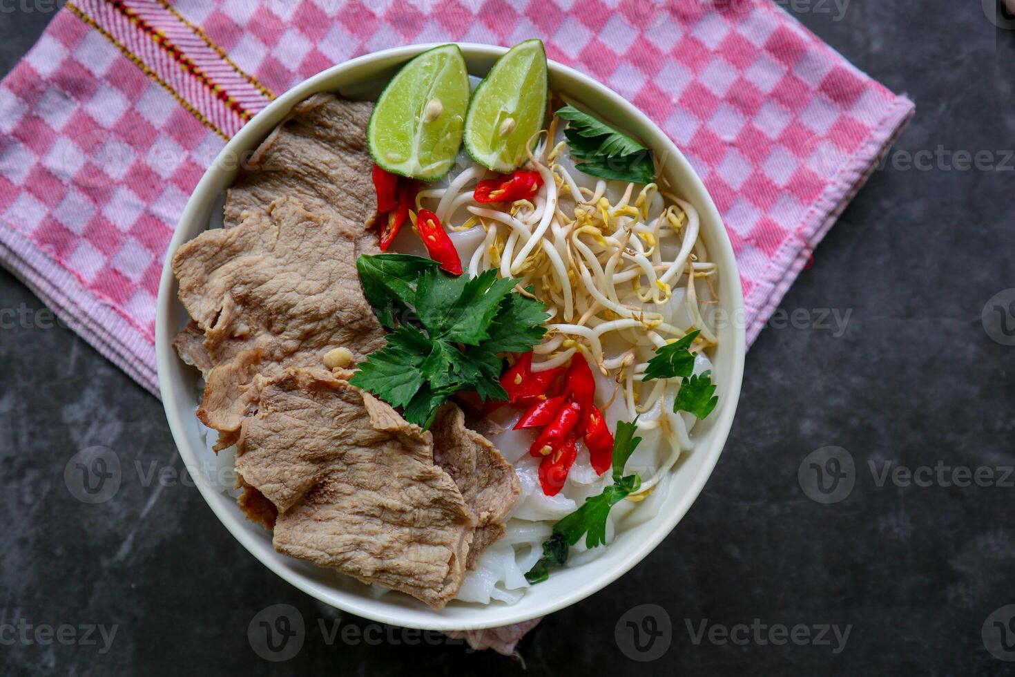 A Bowl Pho Bo traditional Soup with beef, rice noodles, ginger, lime, chili pepper in bowl. Close up. Vietnamese cuisine served on black background photo