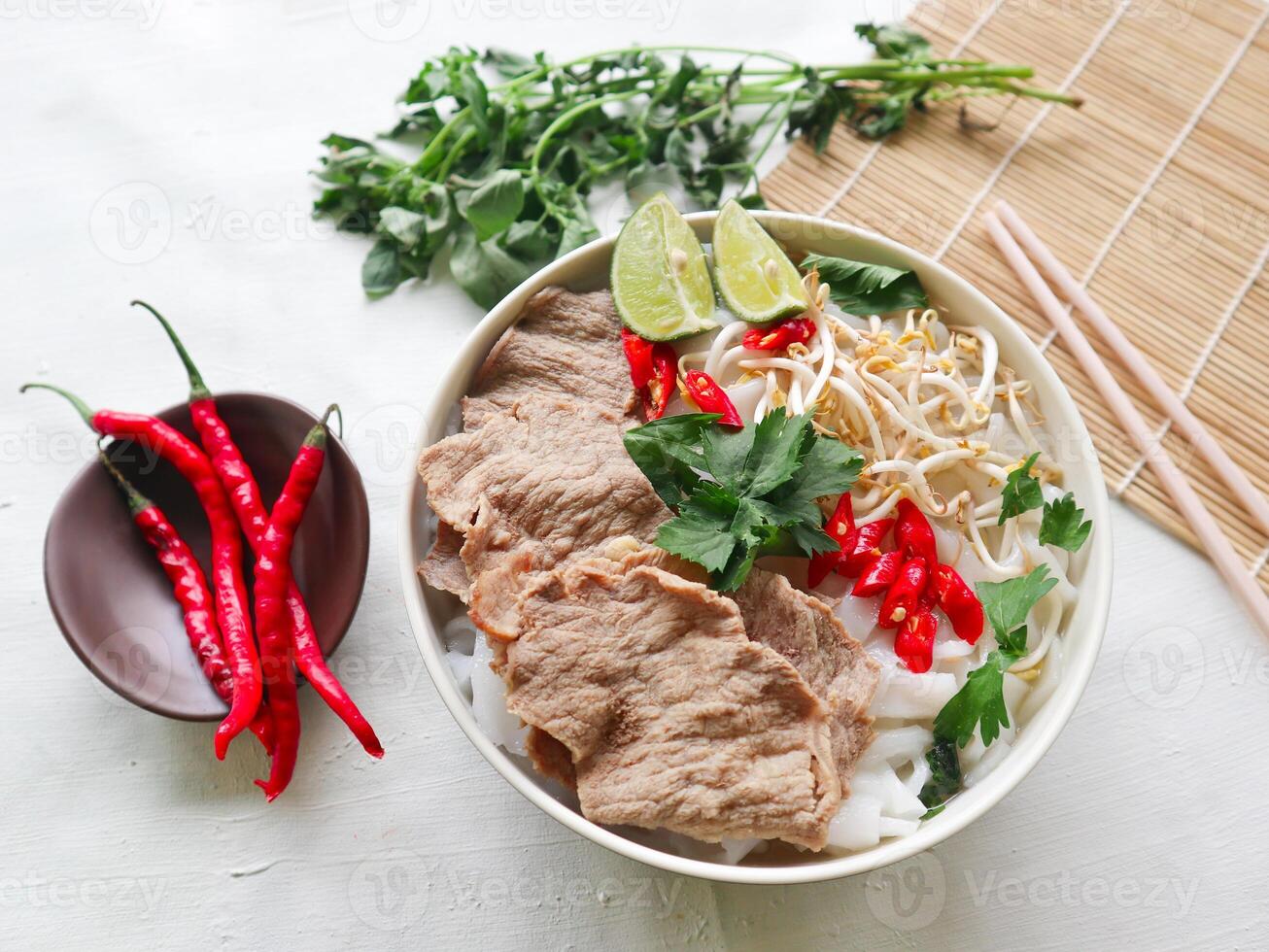 A Bowl Pho Bo traditional Soup with beef, rice noodles, ginger, lime, chili pepper in bowl. Close up. Vietnamese cuisine served on black background photo