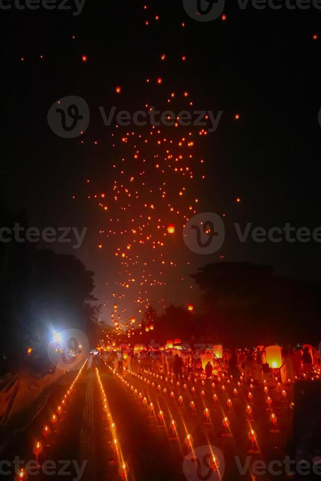 A large group of Buddhist people at Borobudur temple holding burning candles and lanterns. The scene is illuminated with warm, inviting light, creating a festive atmosphere photo