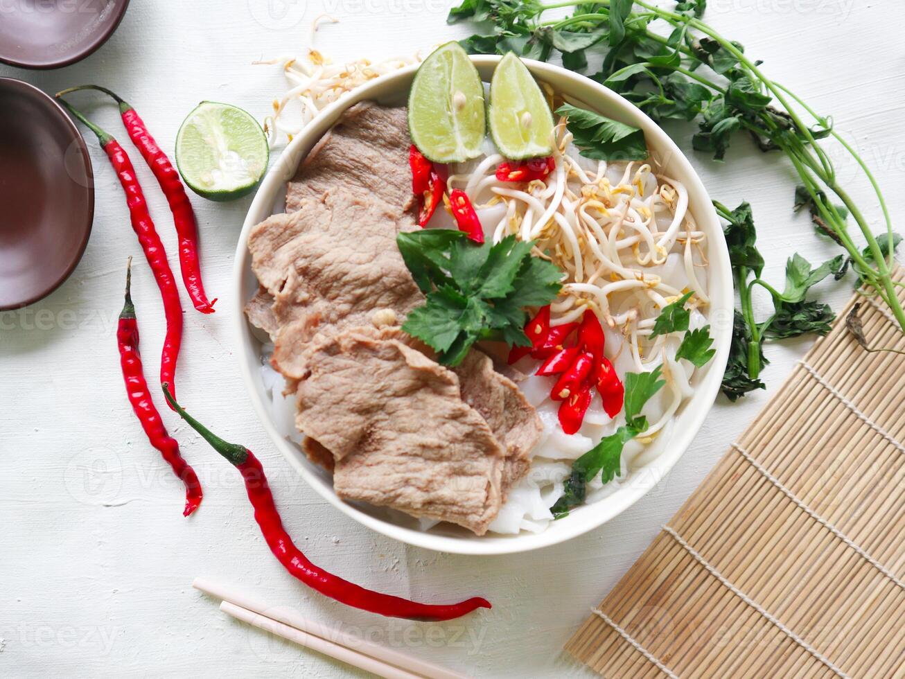 A Bowl Pho Bo traditional Soup with beef, rice noodles, ginger, lime, chili pepper in bowl. Close up. Vietnamese cuisine served on black background photo