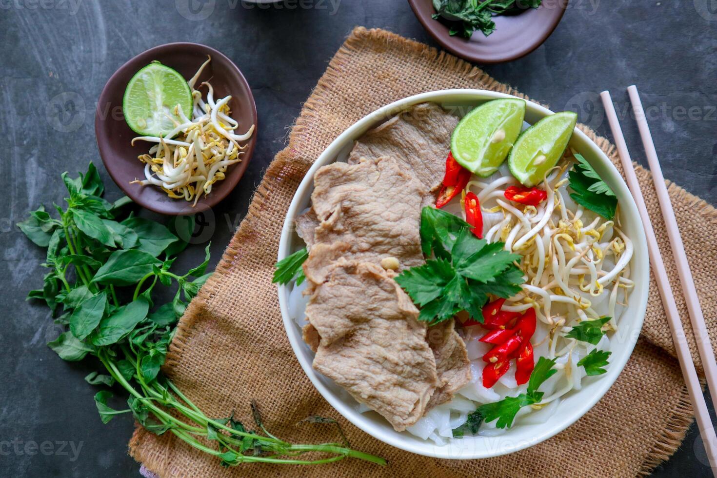 A Bowl Pho Bo traditional Soup with beef, rice noodles, ginger, lime, chili pepper in bowl. Close up. Vietnamese cuisine served on black background photo