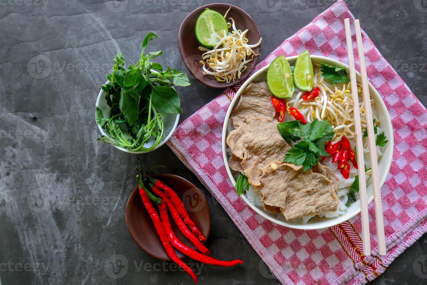 A Bowl Pho Bo traditional Soup with beef, rice noodles, ginger, lime, chili pepper in bowl. Close up. Vietnamese cuisine served on black background photo
