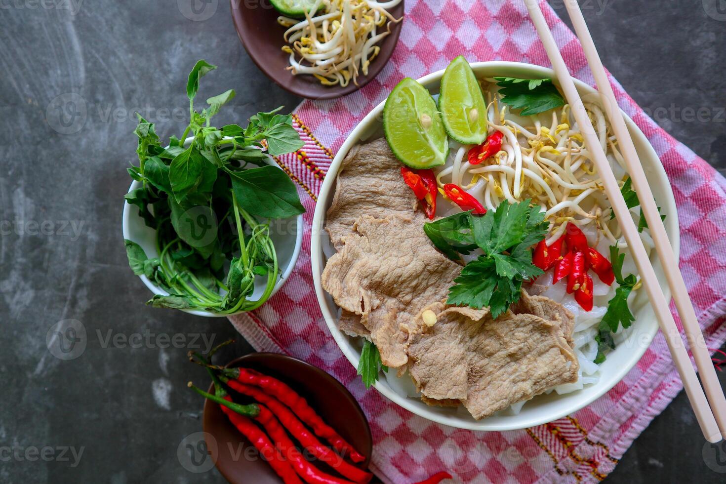 A Bowl Pho Bo traditional Soup with beef, rice noodles, ginger, lime, chili pepper in bowl. Close up. Vietnamese cuisine served on black background photo