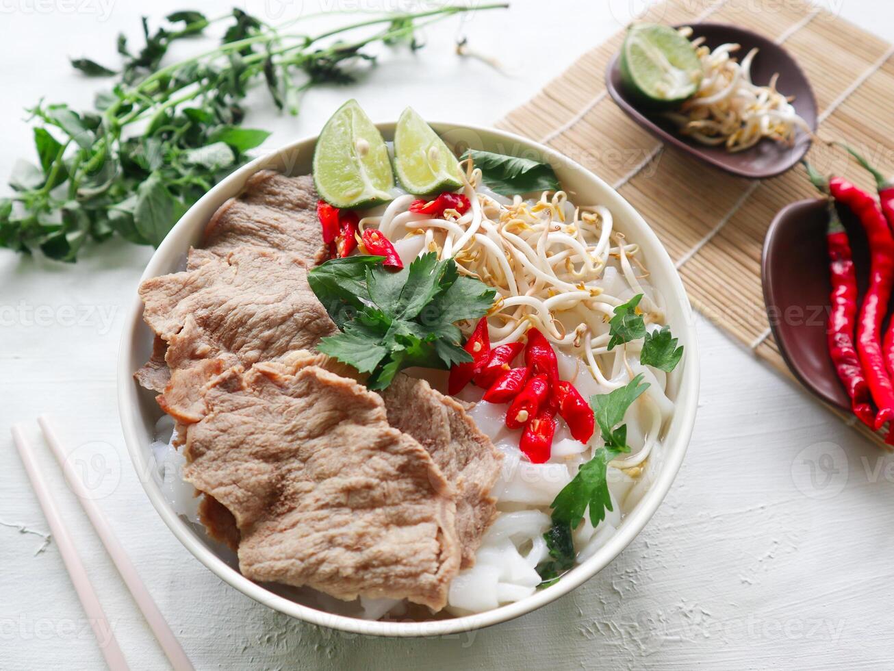 A Bowl Pho Bo traditional Soup with beef, rice noodles, ginger, lime, chili pepper in bowl. Close up. Vietnamese cuisine served on black background photo