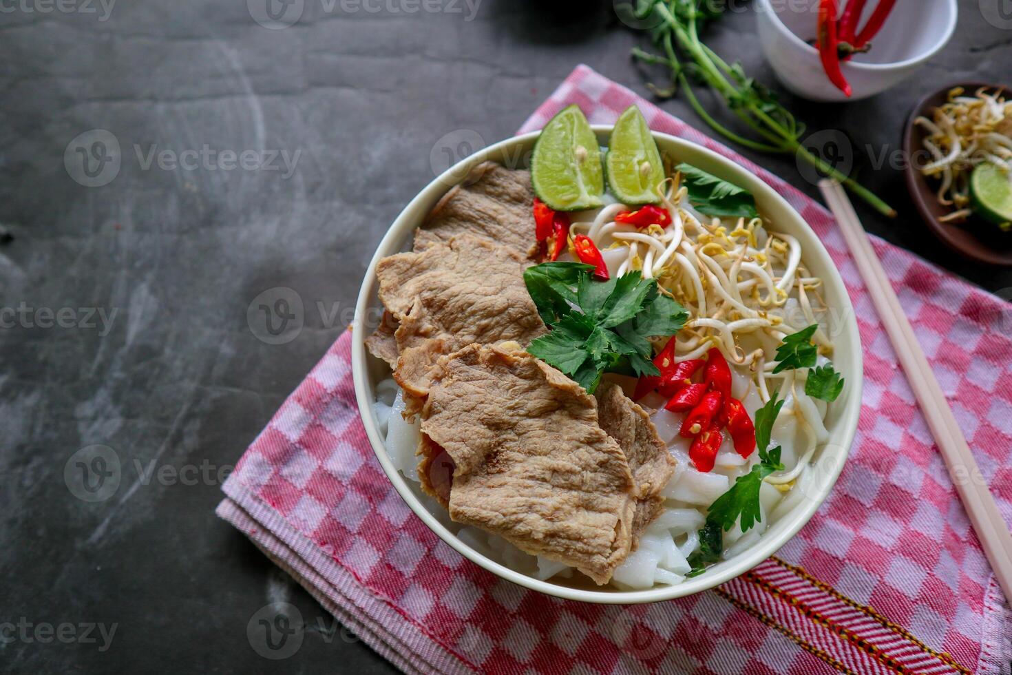 A Bowl Pho Bo traditional Soup with beef, rice noodles, ginger, lime, chili pepper in bowl. Close up. Vietnamese cuisine served on black background photo