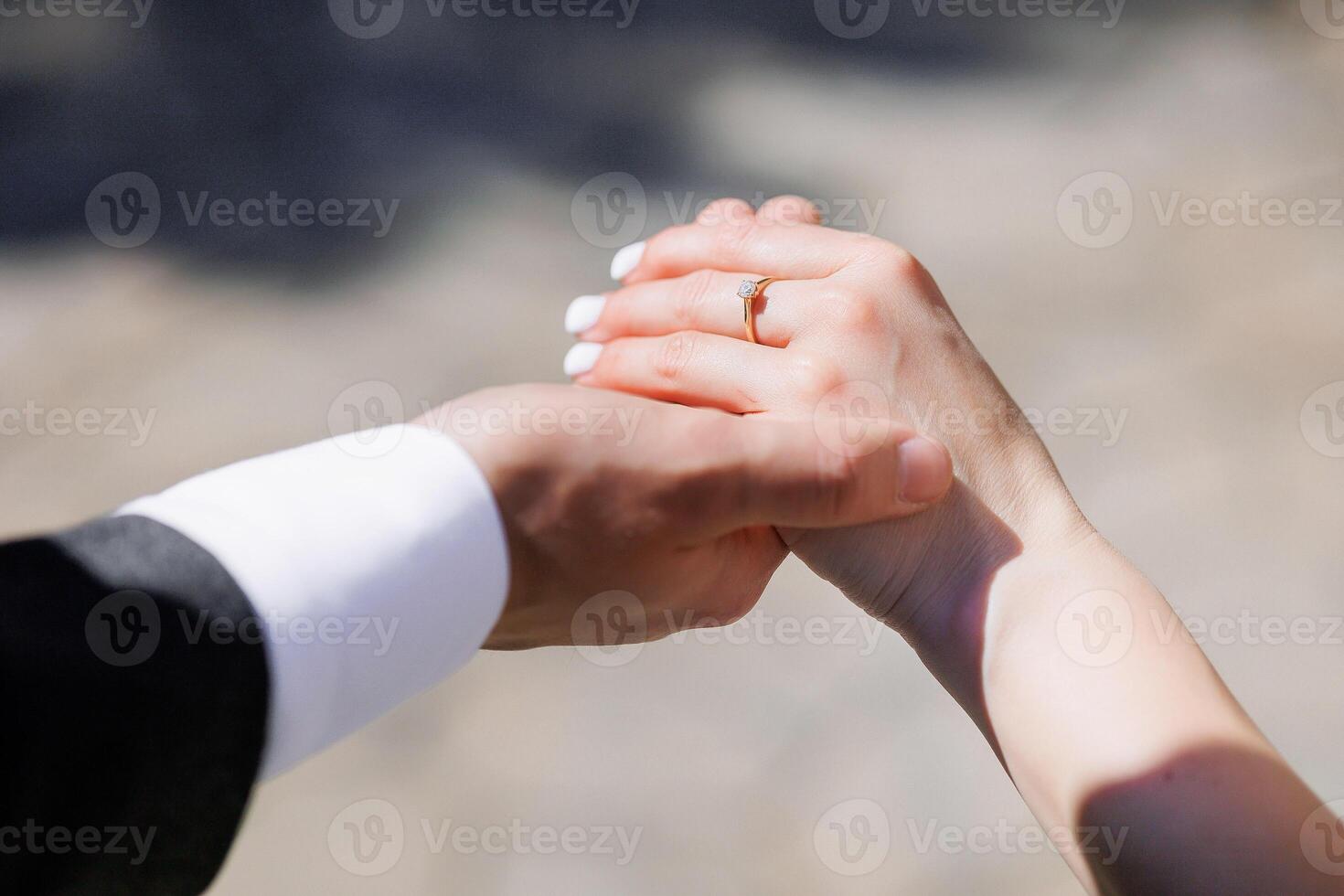 A couple holding hands with a ring on the finger of the woman. The man is wearing a suit and tie photo