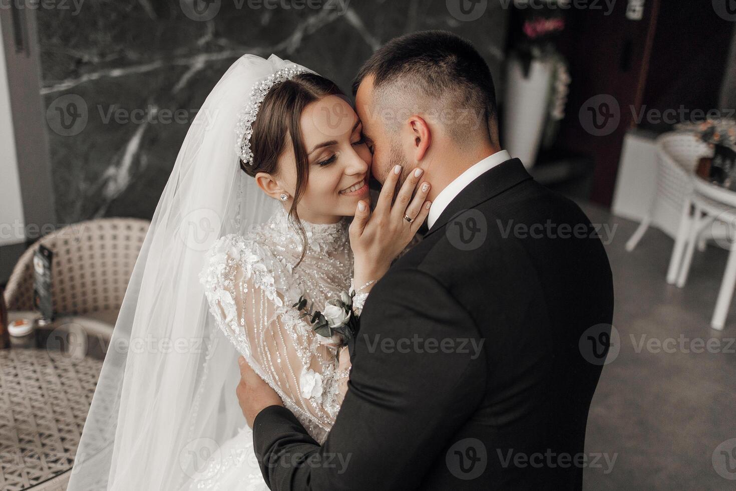 A bride and groom are hugging each other in a black suit and white veil photo