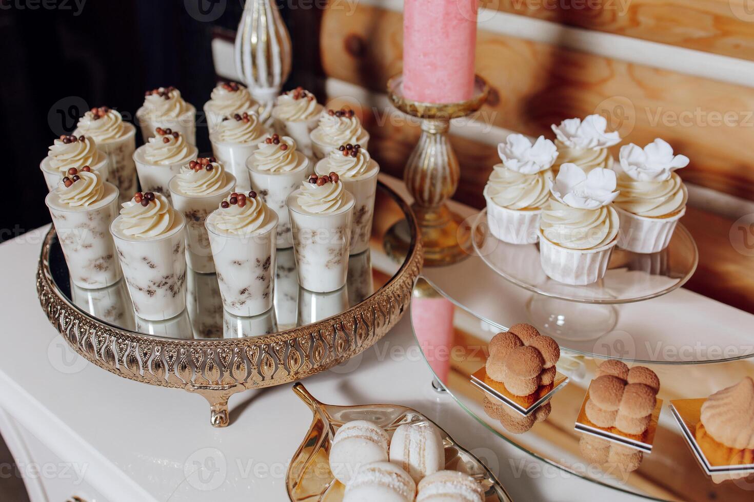 A table with a variety of desserts, including cupcakes and pastries. The desserts are arranged on a silver tray and a white table photo