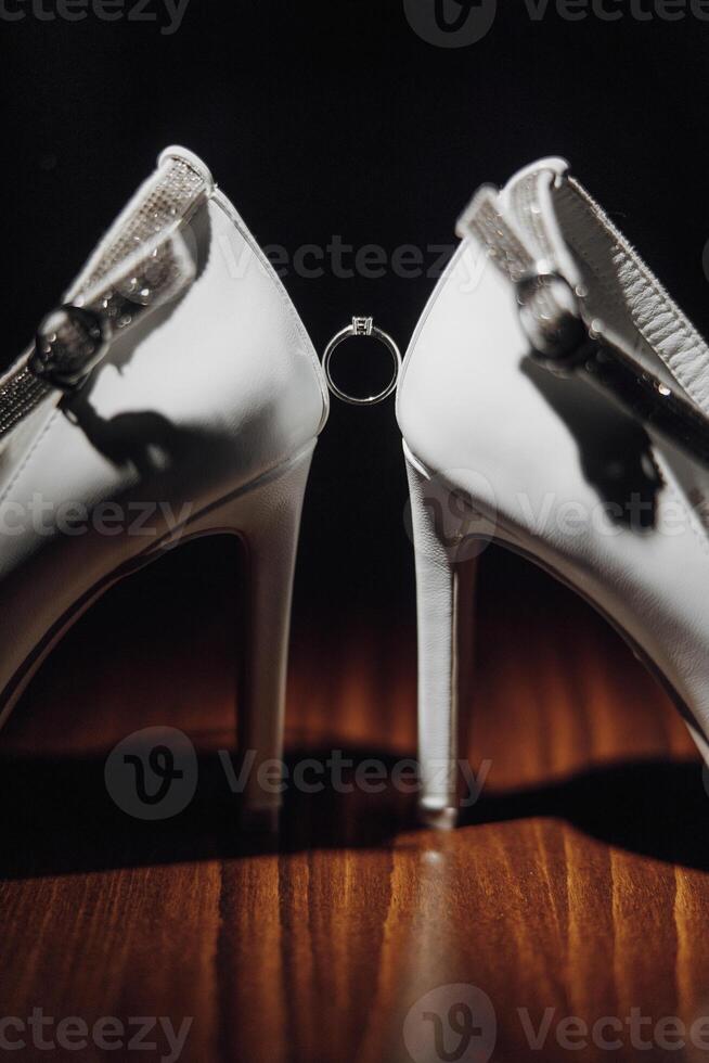 A pair of white shoes with a ring on the toe. The shoes are on a wooden table photo