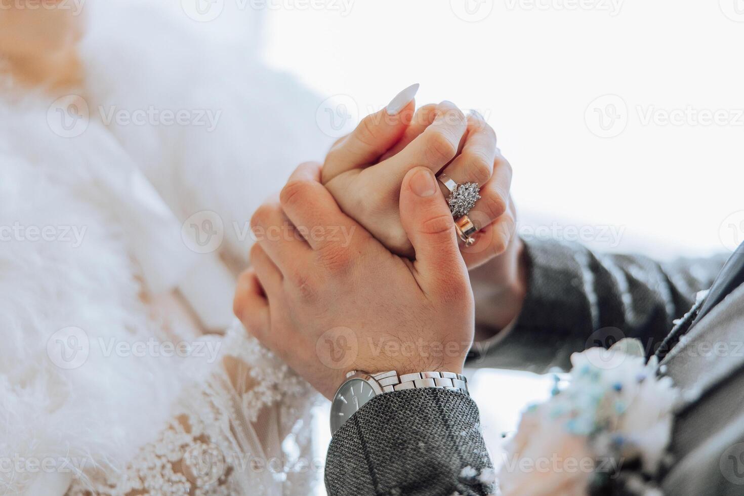 A couple is holding hands and wearing wedding rings. The woman is wearing a white dress and the man is wearing a gray suit. Concept of love and commitment between the couple photo