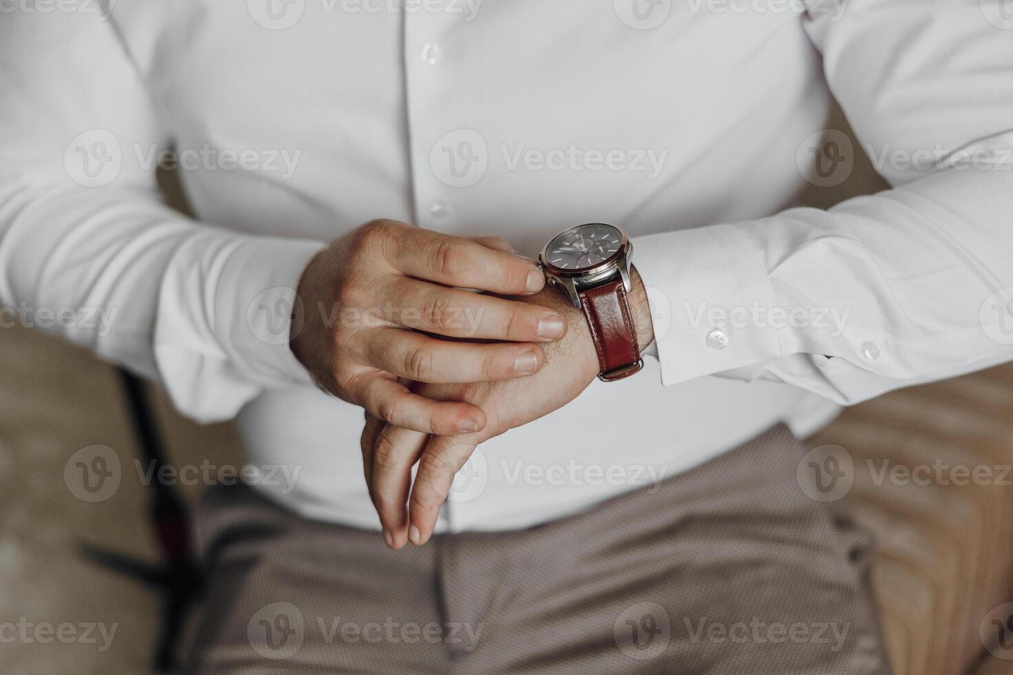 A man is wearing a watch and is checking the time. He is sitting on a couch. The watch is on his left wrist photo