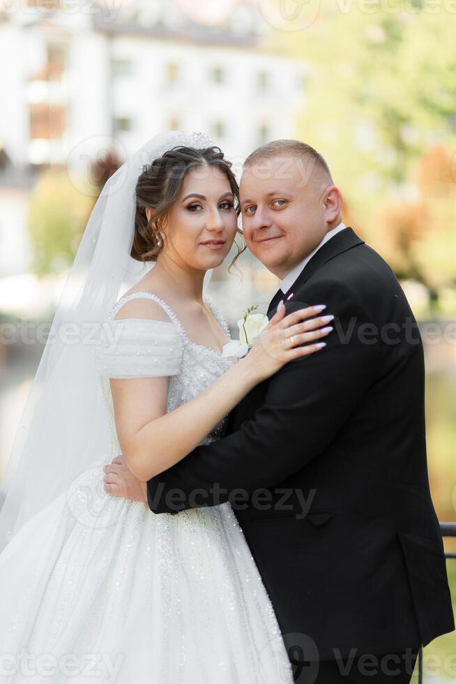 A bride and groom are posing for a picture. The bride is wearing a white dress and the groom is wearing a black suit. They are both smiling and seem happy photo