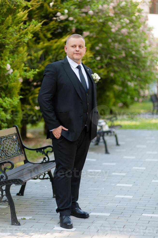 A man in a suit stands in front of a bench, holding a bouquet of flowers. The scene is serene and peaceful, with the man looking confident and poised photo