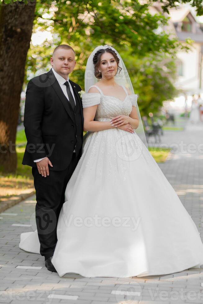 A bride and groom are posing for a picture in front of a tree. The bride is wearing a white dress and the groom is wearing a suit. Scene is happy and celebratory, as the couple is getting married photo
