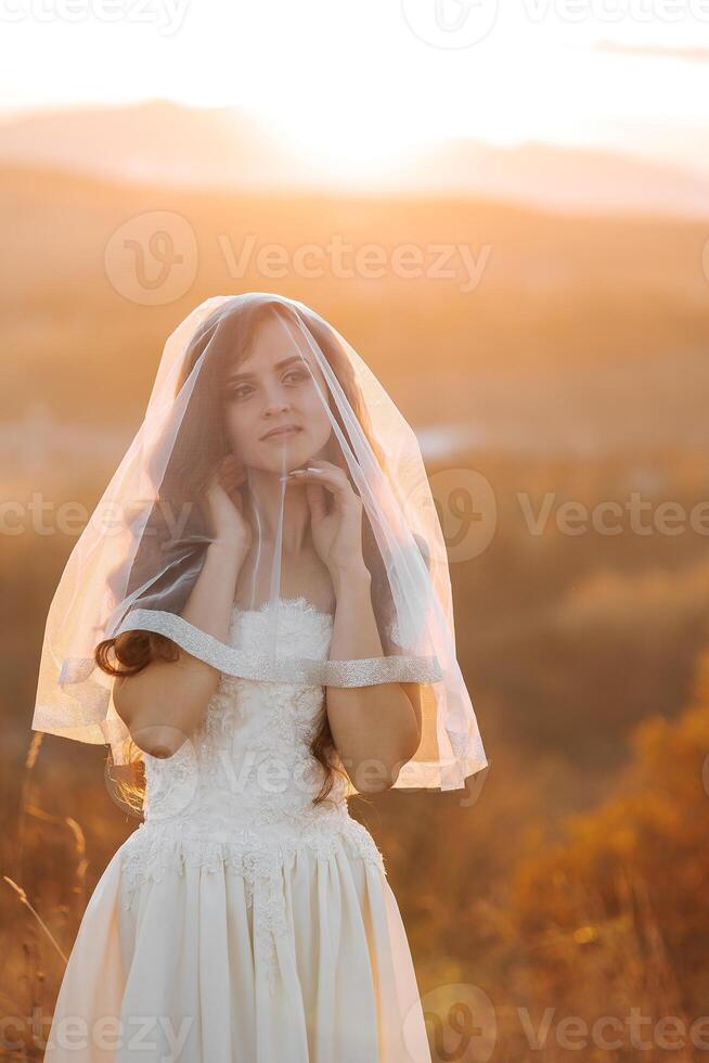 A woman in a white dress is standing in a field with a veil over her face. Concept of mystery and elegance, as the woman's veil obscures her face and adds an air of intrigue to the scene photo