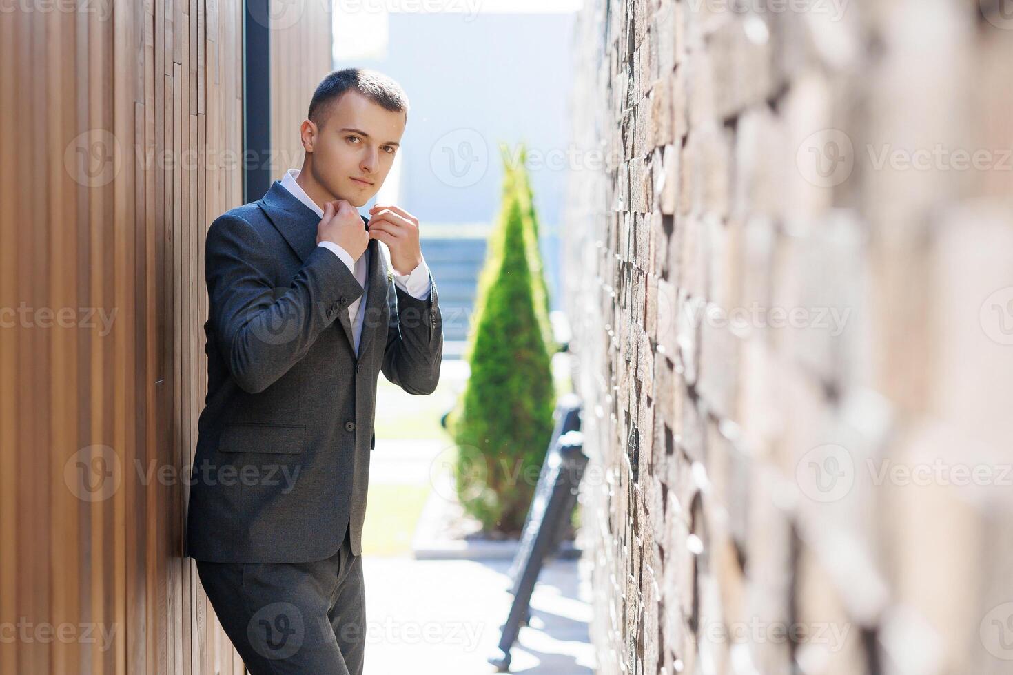 A man in a suit is standing in front of a brick wall. He is wearing a tie and he is getting ready to leave photo