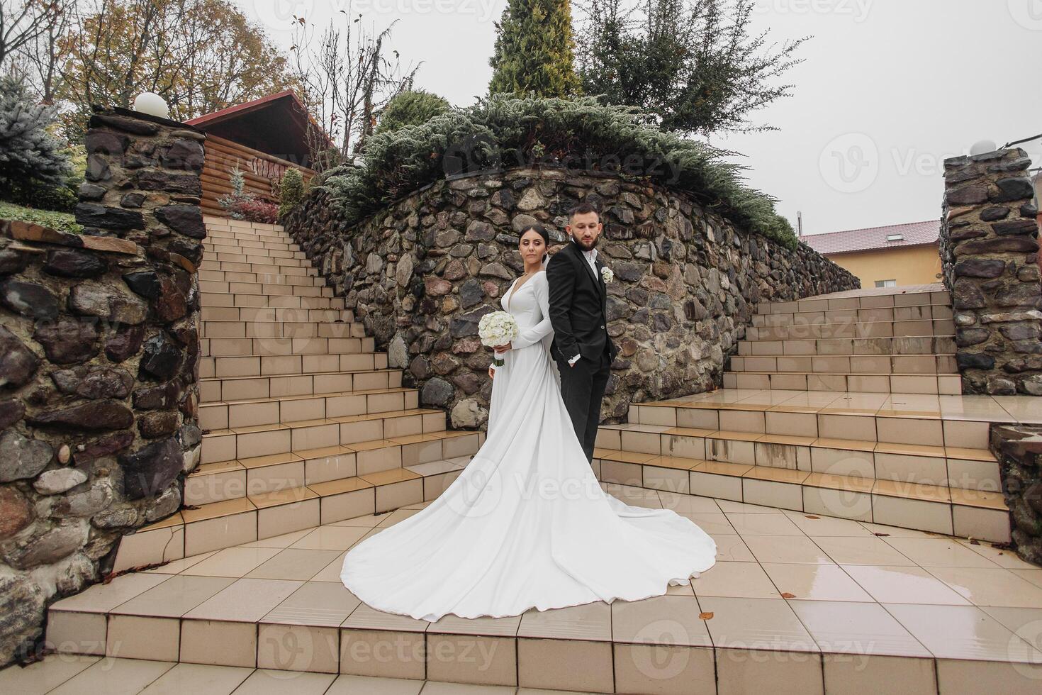 A bride and groom are posing for a picture on a stone staircase. The bride is wearing a white dress and the groom is wearing a suit. Concept of love and commitment photo
