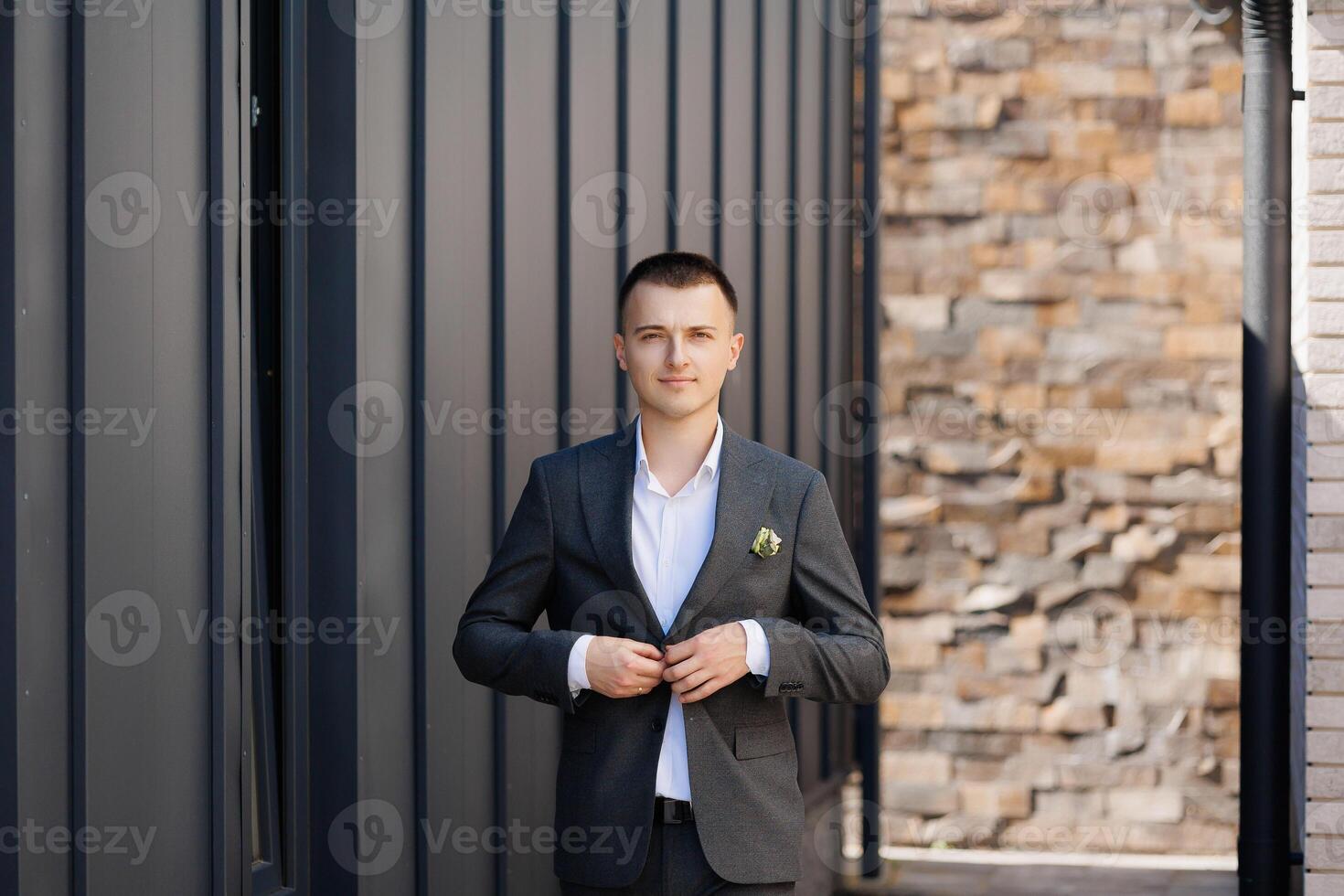 A man in a suit is standing in front of a brick wall. He is wearing a green pin on his lapel photo