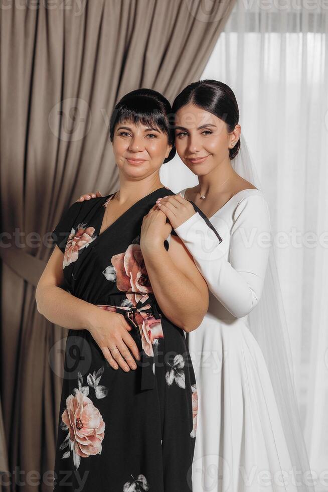 Two women are posing for a picture, one wearing a black floral dress and the other wearing a white dress photo