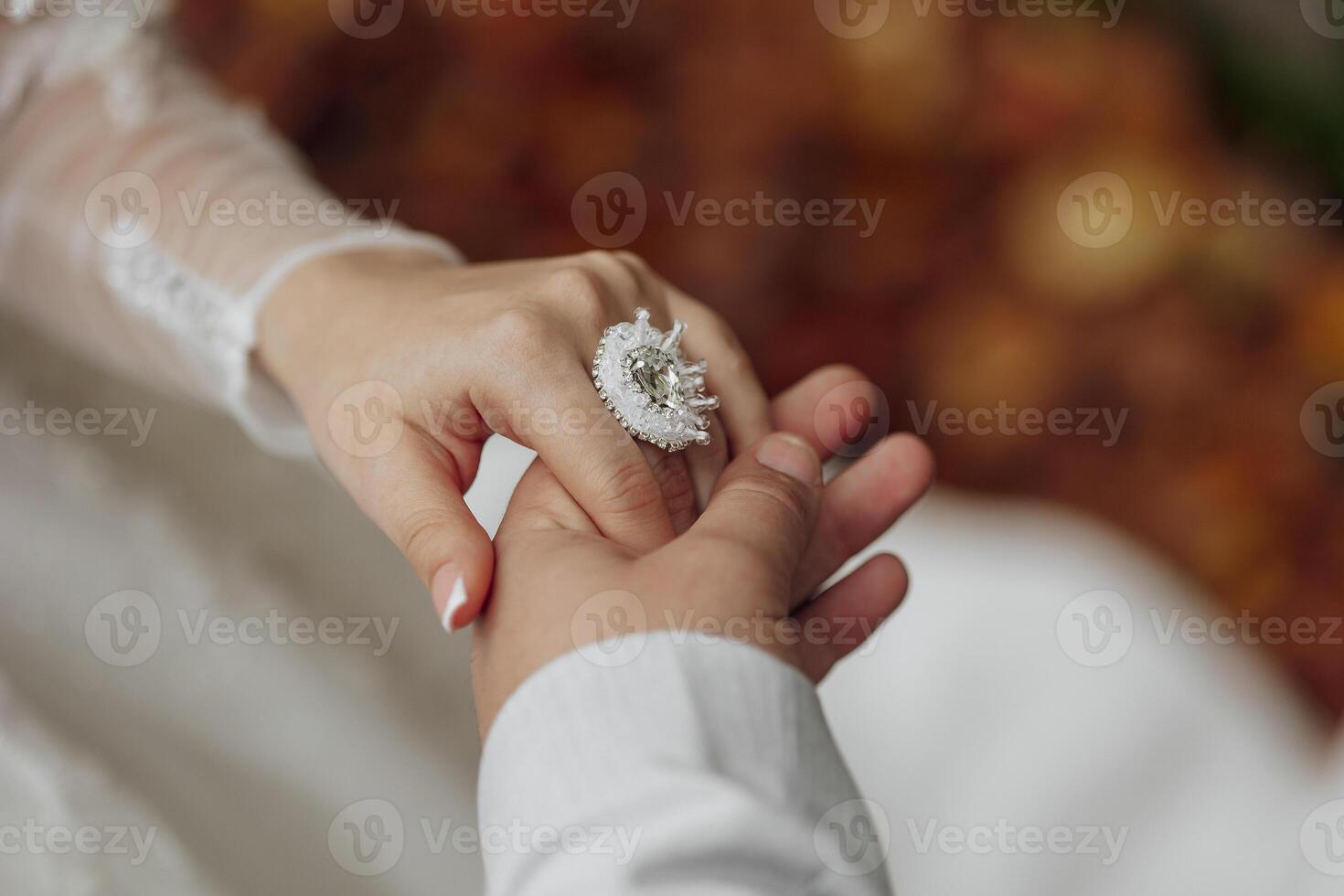 A couple is holding hands and the woman is wearing a ring. The ring is large and has a diamond in the center. Scene is romantic and intimate photo