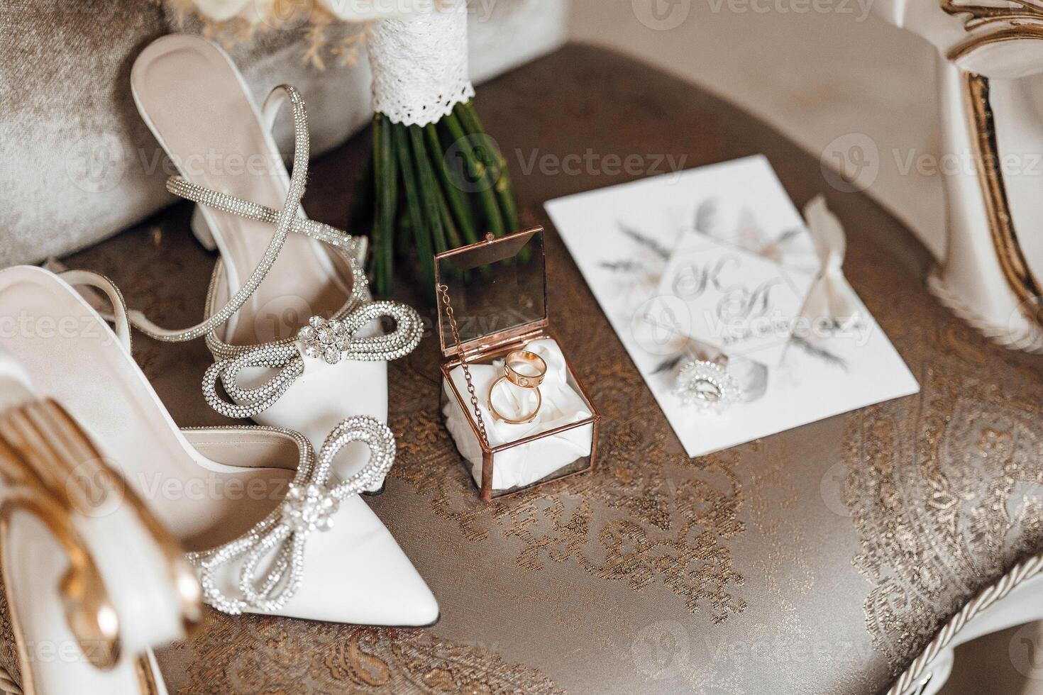 A pair of white shoes with a bow on the front, a ring box, and a bouquet of flowers photo