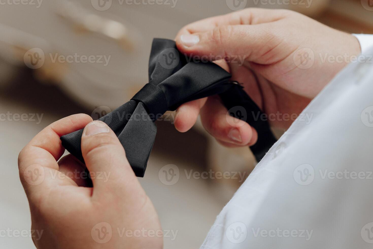 A man is holding a black bow tie and preparing to tie it. Concept of formality and elegance, as the man is getting ready for a special occasion or event photo