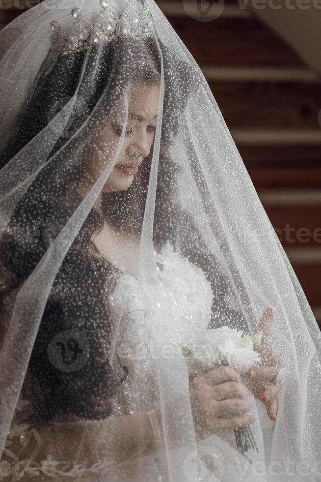 A woman is wearing a veil and holding a bouquet of flowers. She is standing in front of a staircase photo