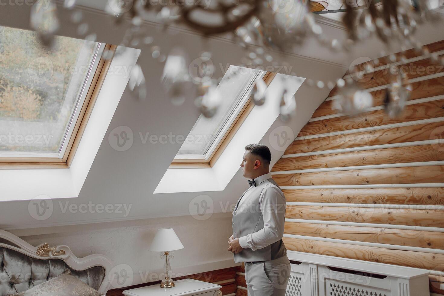 A man in a suit is standing in front of a chandelier. The room has a warm and inviting atmosphere photo