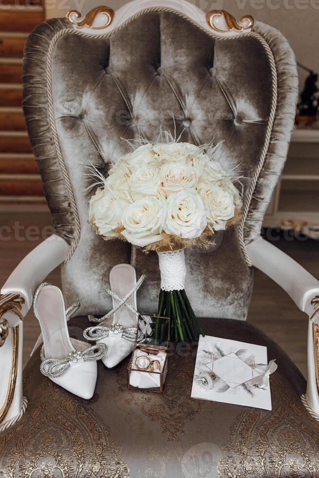 A chair with a bouquet of white roses and a pair of white shoes on it. The chair is surrounded by other items, including a box and a card photo
