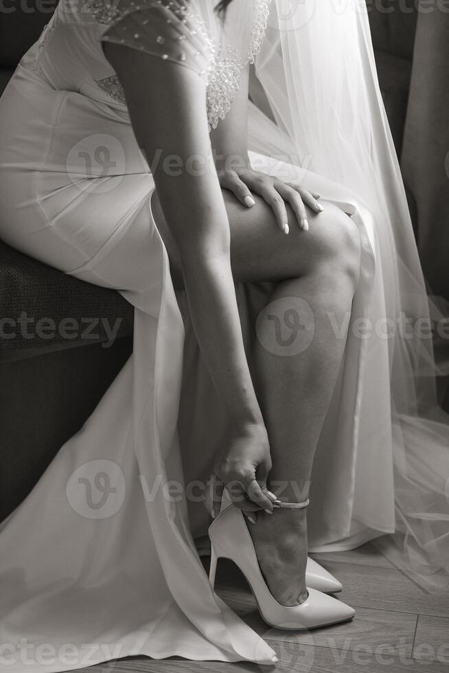 A woman in a wedding dress sits on a couch, putting on her shoes. Concept of elegance and sophistication, as the woman is dressed in a formal gown and is taking care to put on her shoes properly photo