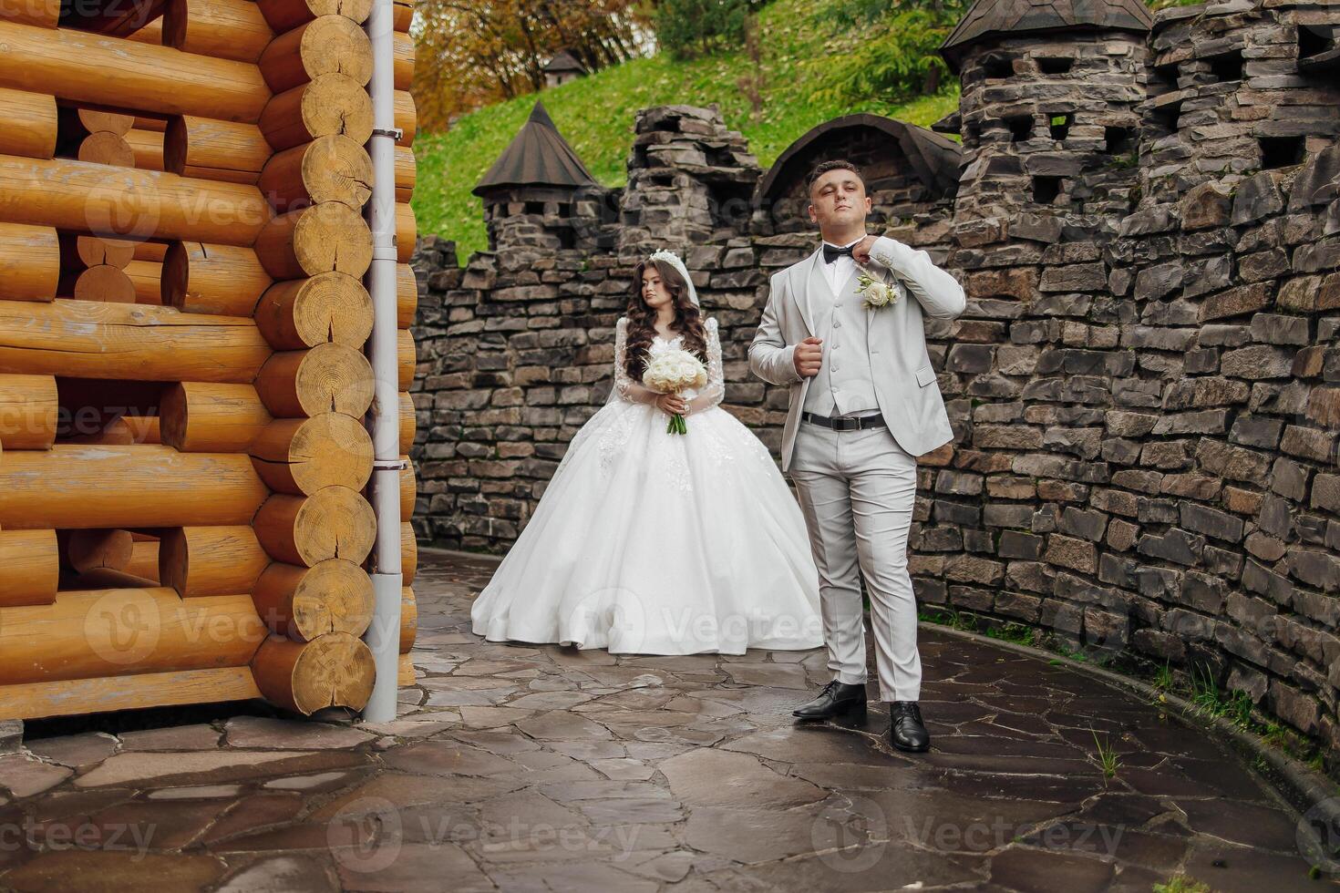 A bride and groom stand in front of a castle, with the bride holding a bouquet photo