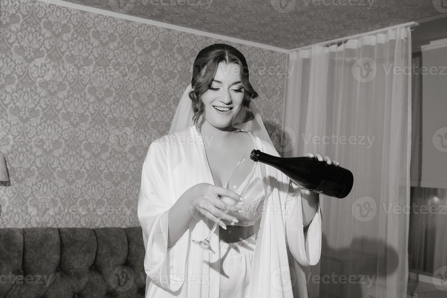 A woman in a white robe is pouring wine into a glass. She is smiling and she is enjoying the moment photo
