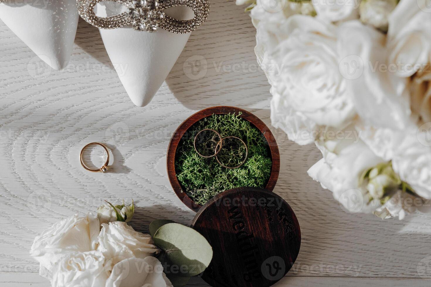 A wooden box with two rings inside sits on a table next to a vase of white flowers photo