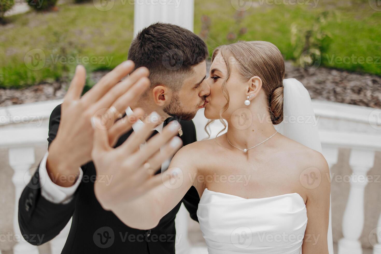 A bride and groom kiss each other's hands in a wedding photo. The bride is wearing a white dress and the groom is wearing a suit photo